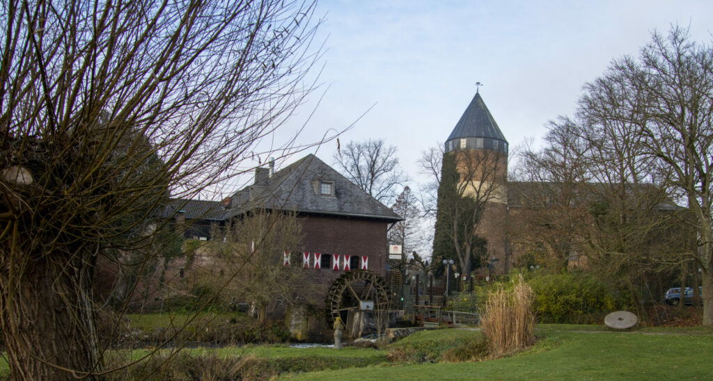 Die Burg Brüggen und ihre Mühle an der Schwalm vor regionaltypischen Kopfweiden.